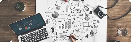 Top view of a business strategy planning workspace with hand-drawn ideas, charts, and a laptop